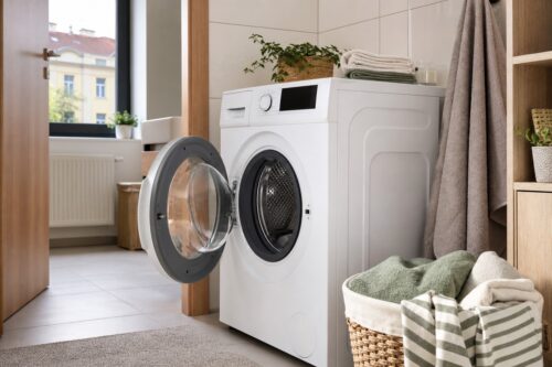 Čistá moderní pračka v koupelně s otevřenými dvířky a košem na ručníky